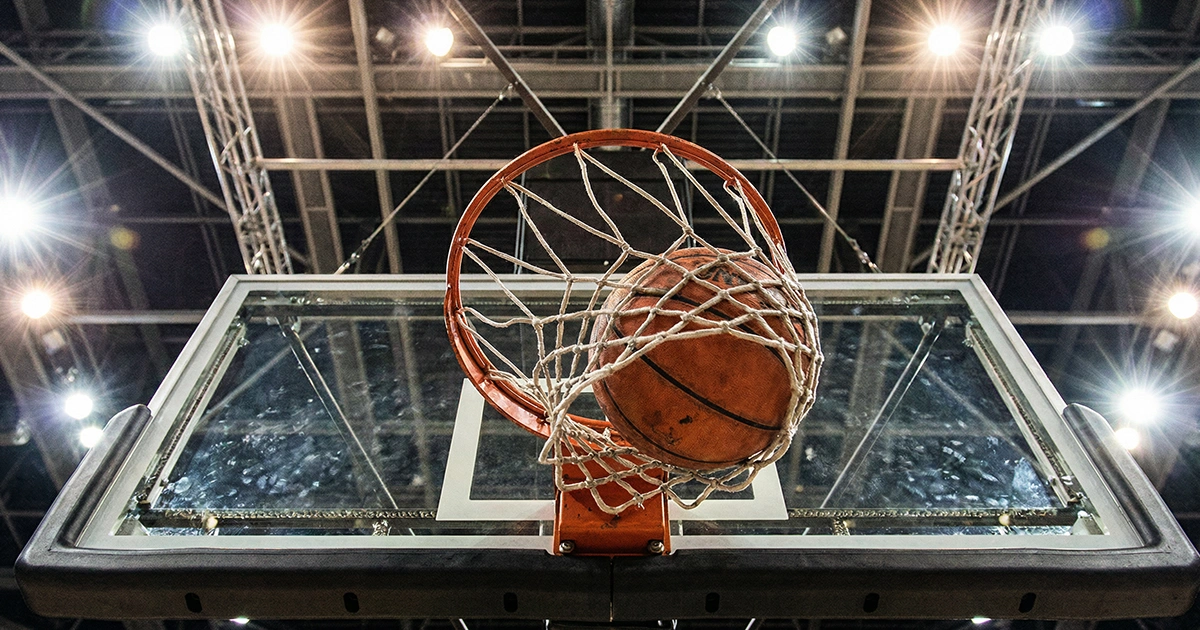 Canasta de baloncesto vista desde abajo con el balón entrando por el aro en un pabellón iluminado